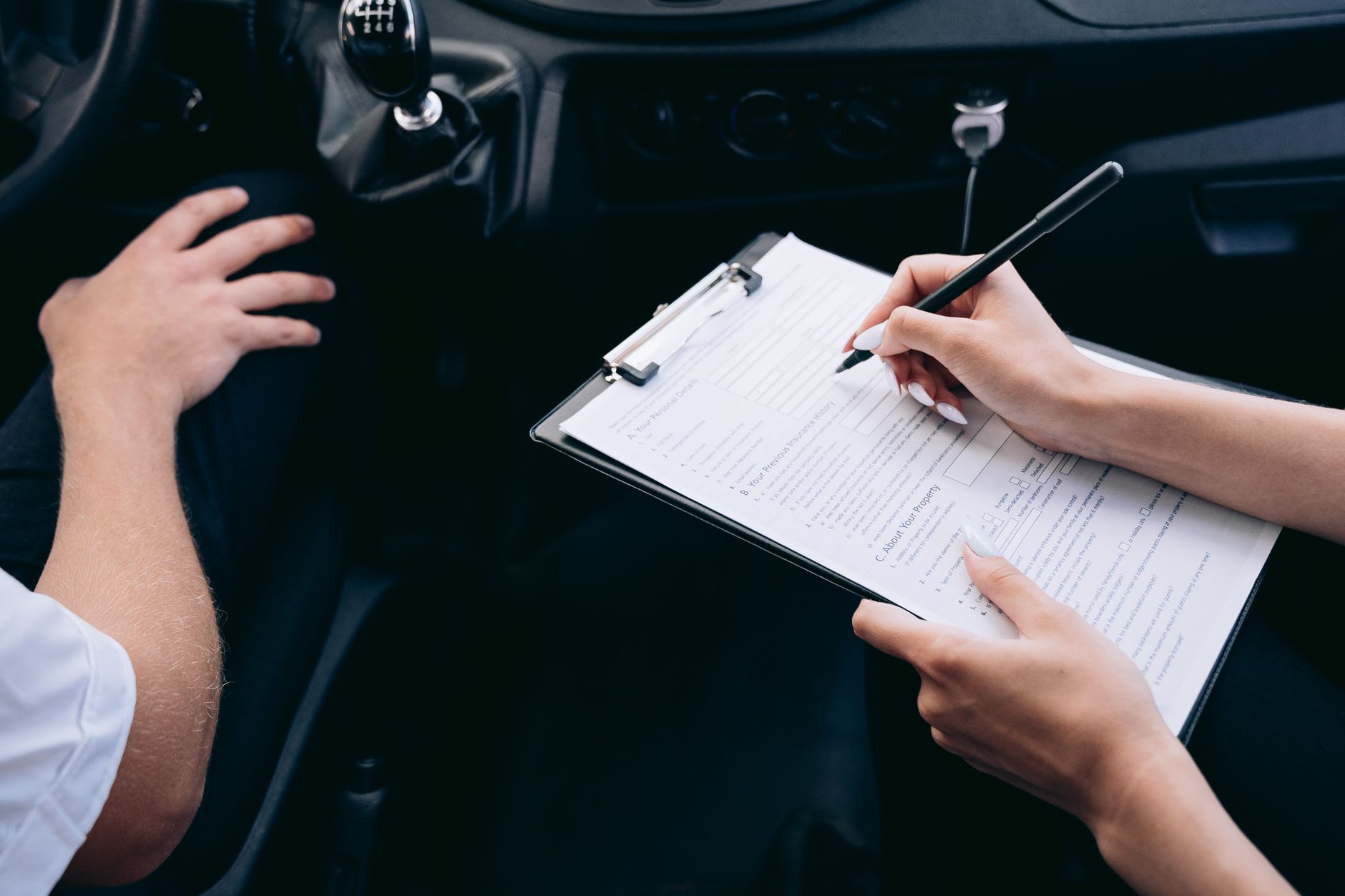 Mãos preenchendo uma prancheta ao lado do carro